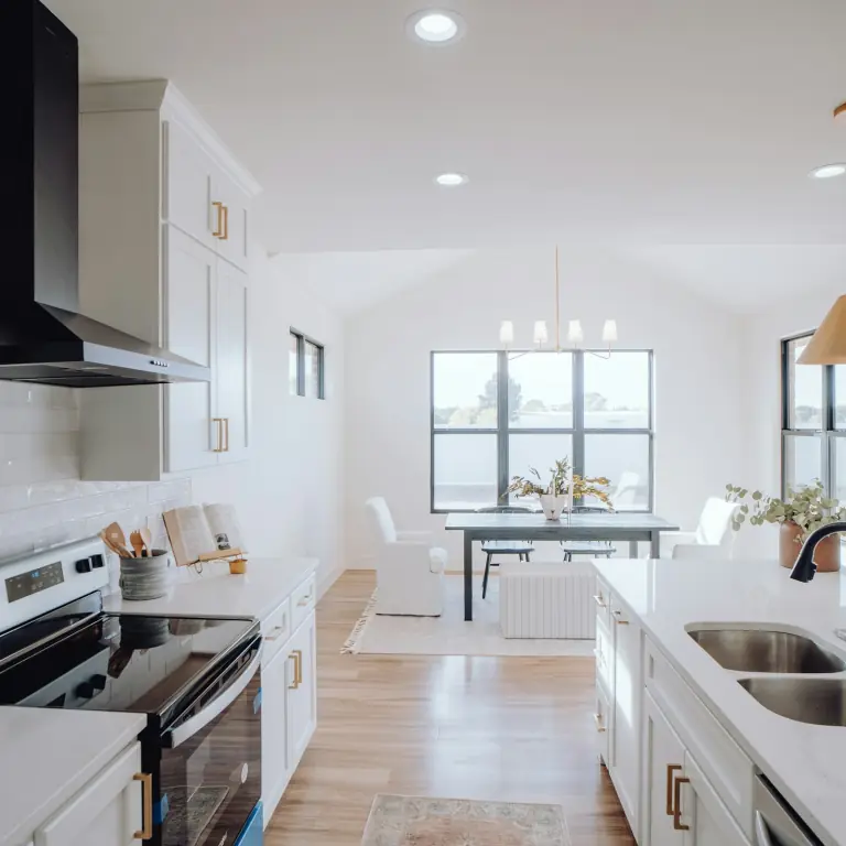 White shaker kitchen with brass pulls, a black range hood, a quartz island with a matte black faucet and a dining nook under black-framed windows