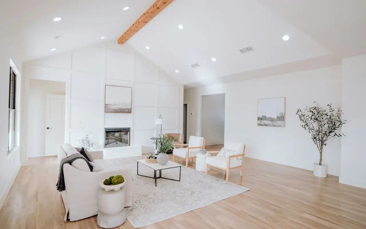 Vaulted great room with a cedar beam, a panelled fireplace wall, a slipcovered sofa, two oak armchairs and light oak floors