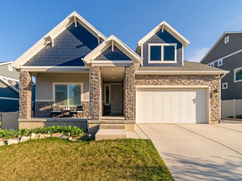 Craftsman-style home with navy shingle gables, stacked stone columns, a covered front porch with two chairs and a double garage