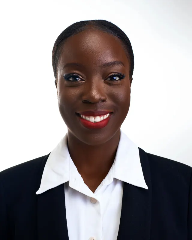 Woman with her hair pulled back, smiling, in a black blazer over a white shirt against a white backdrop