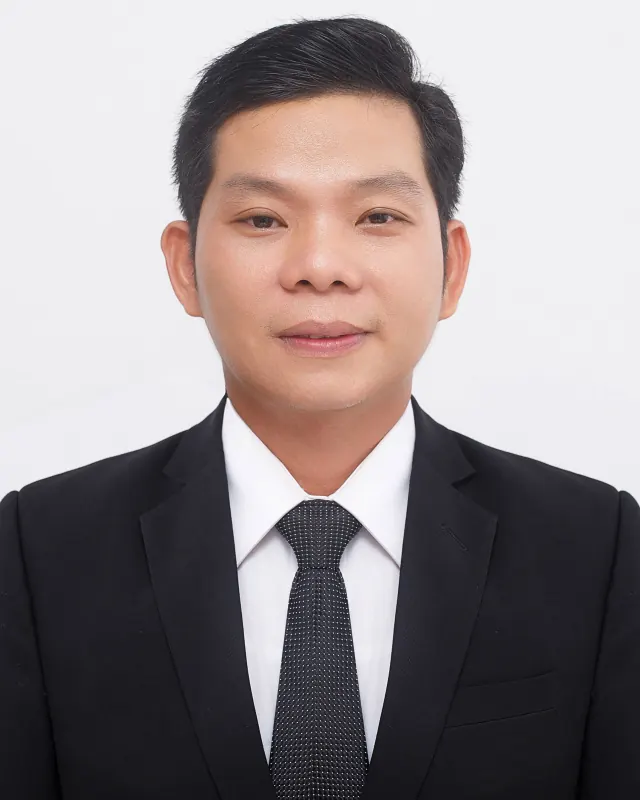 Man with short dark hair in a dark suit, white shirt and patterned tie against a white backdrop